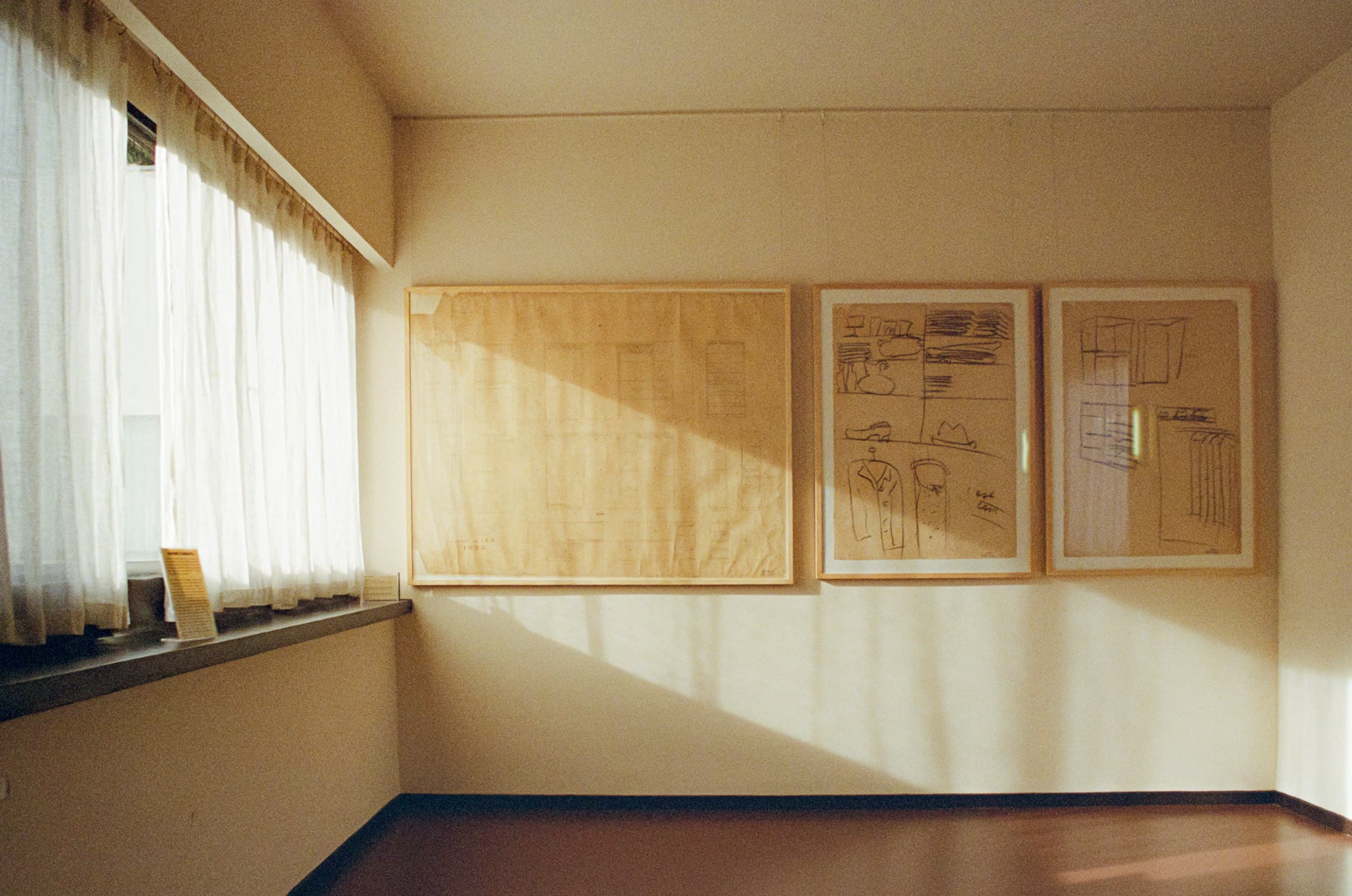 Sunlit room with sheer curtains and framed design drawings along a warm plaster wall