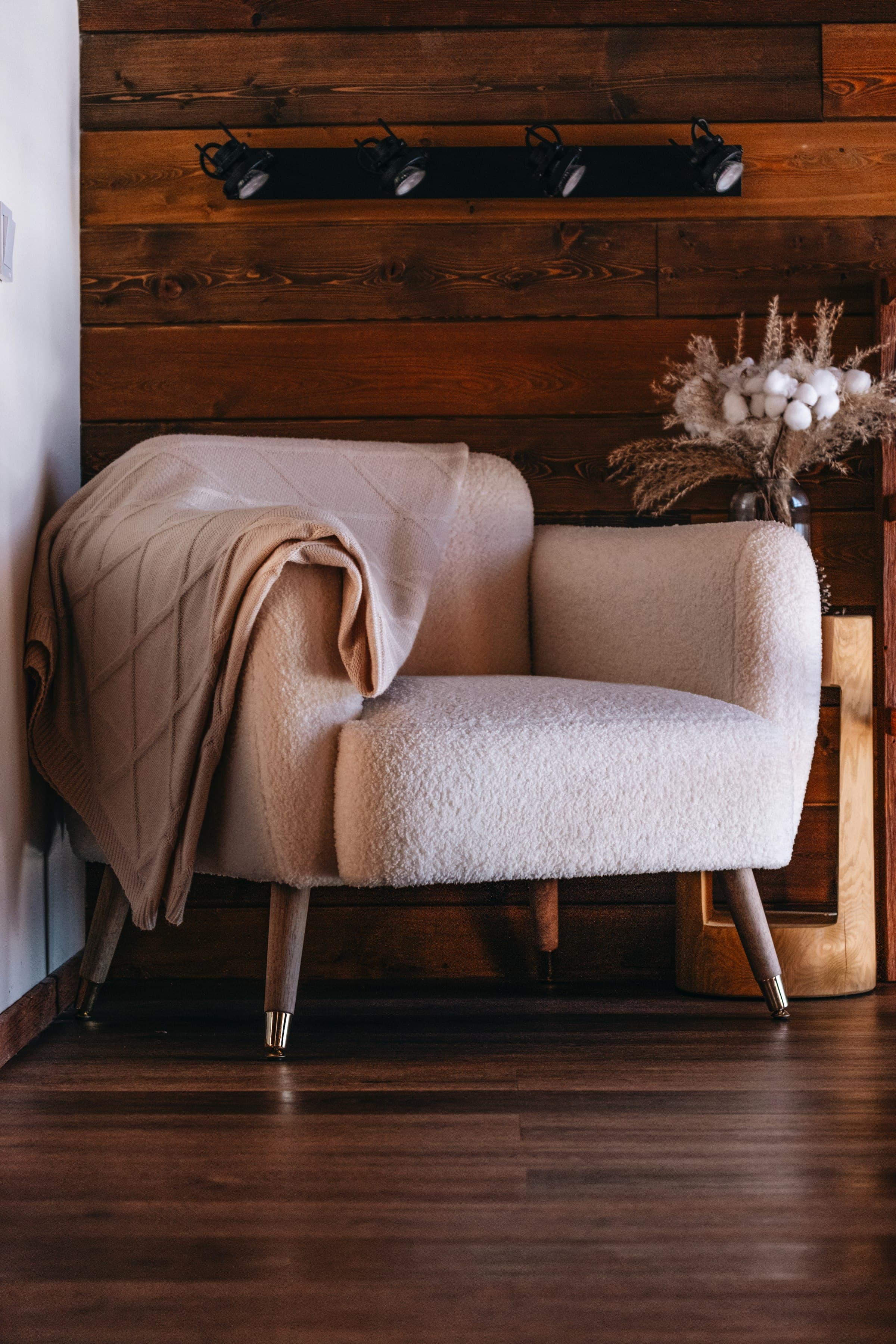Bouclé armchair with a knitted throw on a dark wooden floor