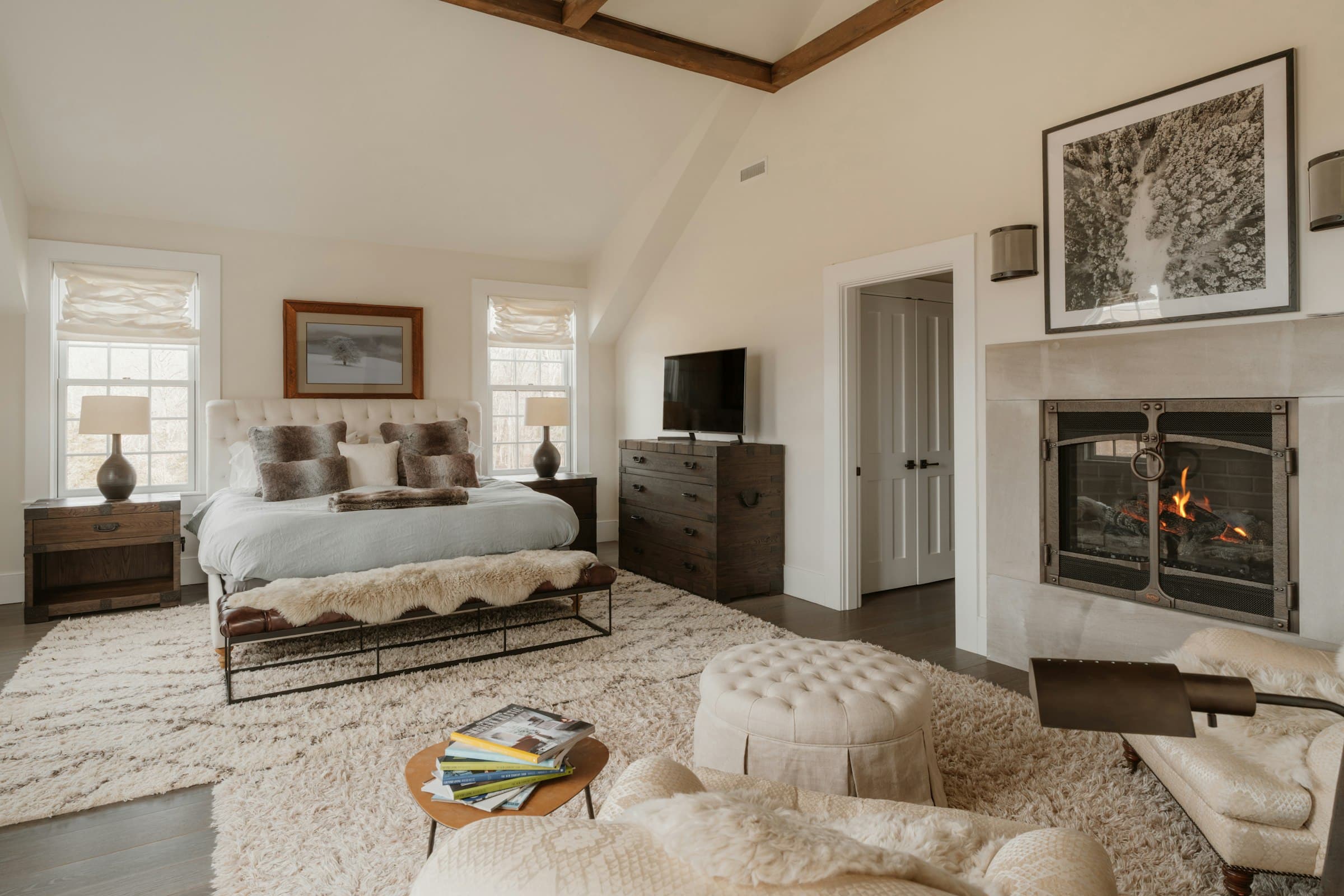 Bright bedroom with a fireplace, an upholstered bed, a textured rug and a tufted ottoman